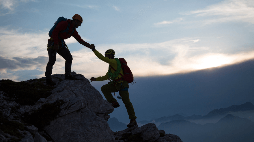 One mountain climber helps another up onto a mountain top.